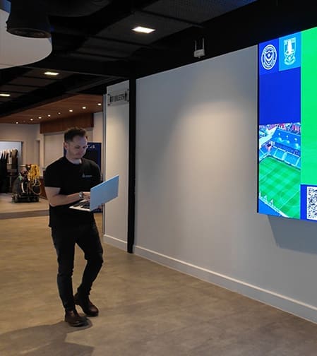 man holding a laptop in front of a large screen